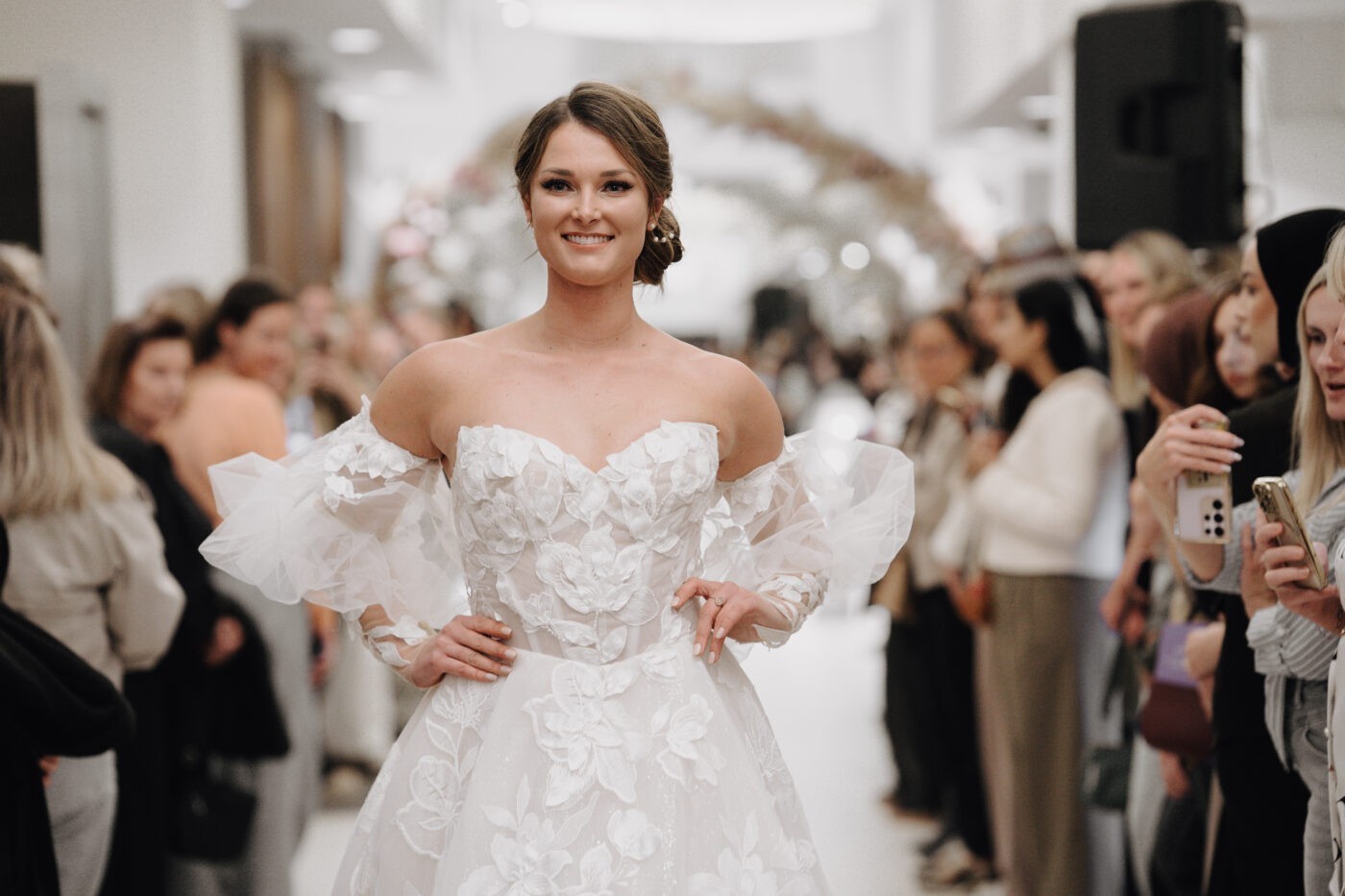 Model in trouwjurk op catwalk weddingshow. Strapless trouwjurk van kant met pof mouwen